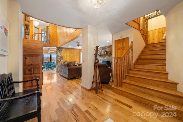 stairs featuring ceiling fan, hardwood / wood-style floors, a stone fireplace, and wooden walls