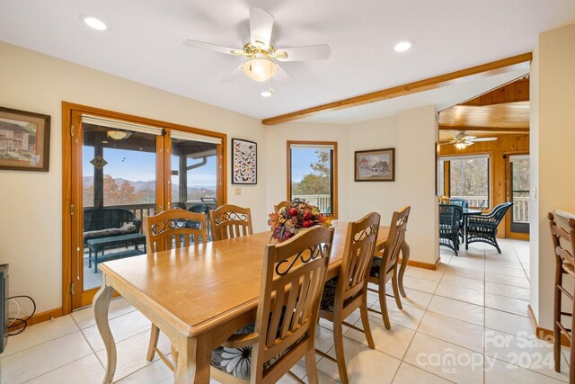 dining space featuring light tile patterned flooring, wooden walls, beam ceiling, and ceiling fan