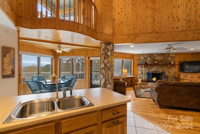 kitchen featuring a fireplace, wooden walls, sink, light tile patterned flooring, and ceiling fan