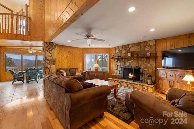 living room featuring ceiling fan, light wood-type flooring, beam ceiling, a fireplace, and wood walls