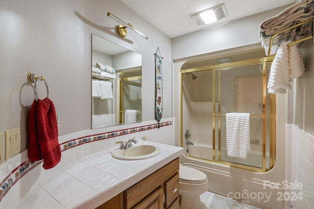 full bathroom with combined bath / shower with glass door, vanity, and toilet