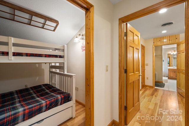 bedroom with light hardwood / wood-style floors, vaulted ceiling, and ensuite bathroom