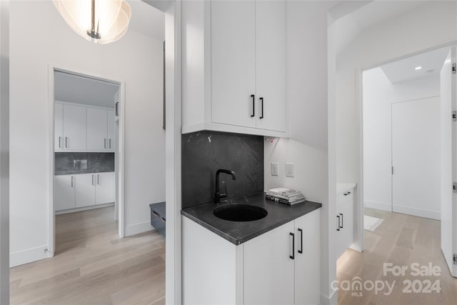 kitchen with light wood-type flooring, white cabinetry, sink, and backsplash