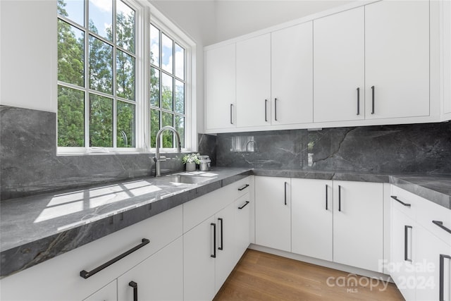 kitchen featuring wood-type flooring, white cabinetry, dark stone countertops, and sink