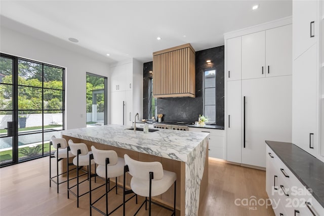 kitchen with white cabinets, sink, tasteful backsplash, a kitchen island with sink, and light hardwood / wood-style flooring