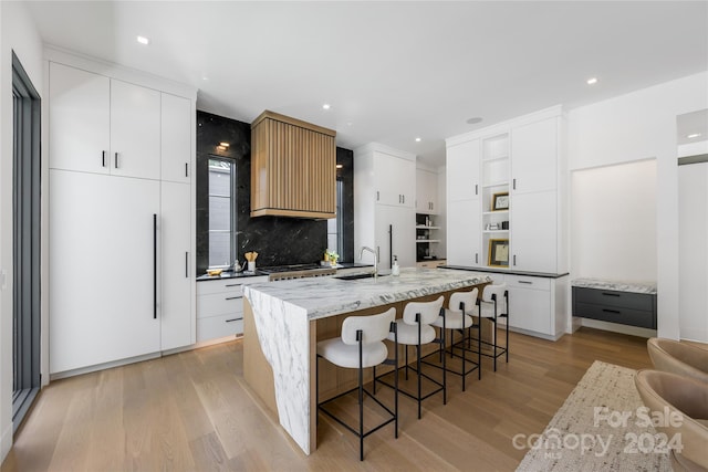 kitchen featuring light hardwood / wood-style floors, white cabinetry, backsplash, a kitchen bar, and a kitchen island with sink