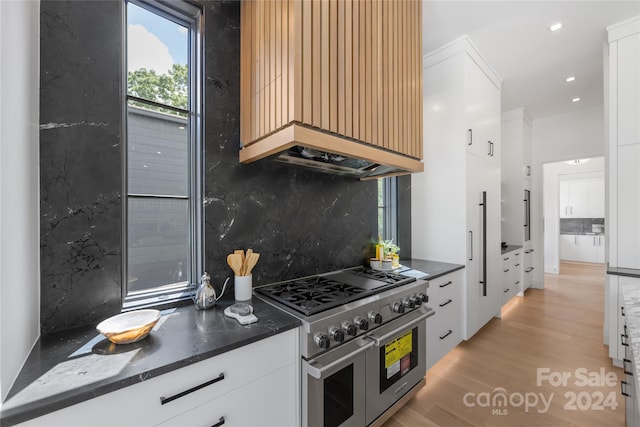 kitchen with tasteful backsplash, white cabinetry, light hardwood / wood-style flooring, range with two ovens, and dark stone countertops