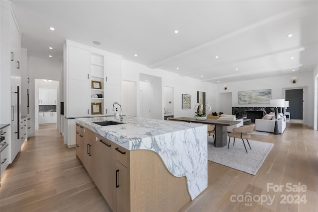 kitchen featuring light wood-type flooring, light stone counters, sink, an island with sink, and a fireplace