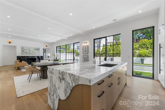 kitchen featuring light hardwood / wood-style floors, beam ceiling, a spacious island, sink, and a premium fireplace