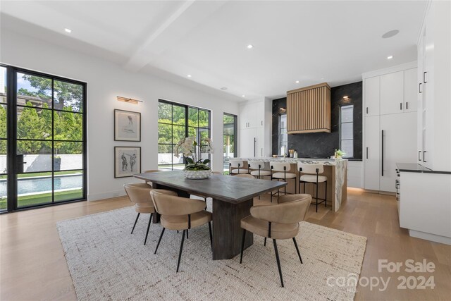 dining space with light wood-type flooring, beam ceiling, and a healthy amount of sunlight