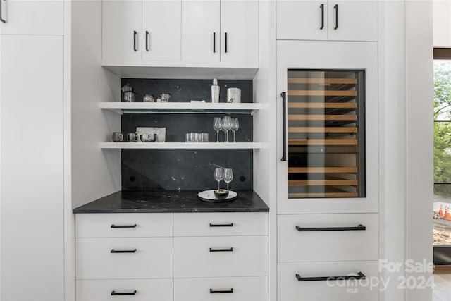 bar with dark stone countertops, white cabinets, beverage cooler, and decorative backsplash