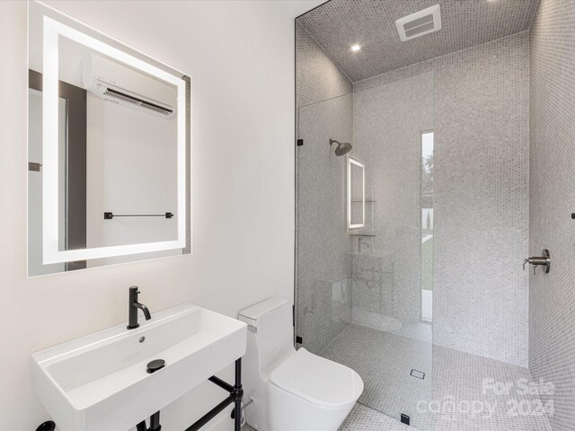 bathroom with a tile shower, a wall unit AC, toilet, and sink