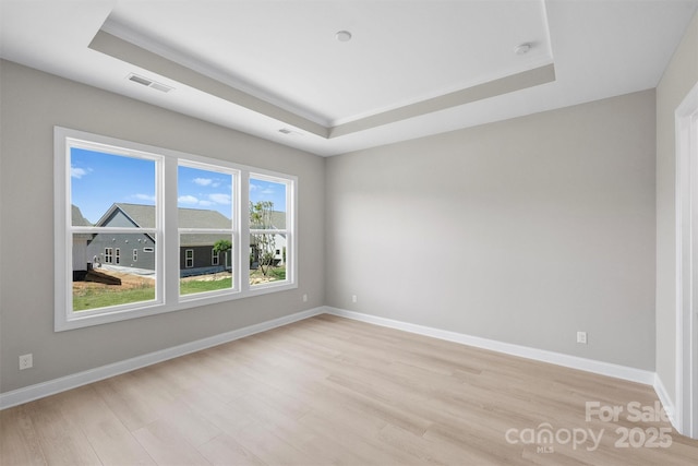 unfurnished room featuring light wood-style floors, baseboards, visible vents, and a raised ceiling