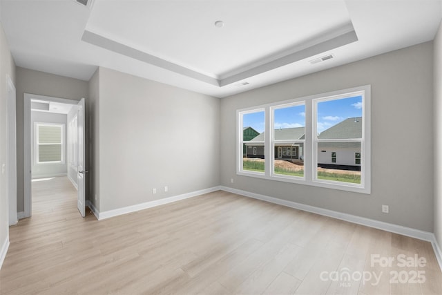 empty room featuring light wood-type flooring, a raised ceiling, and visible vents