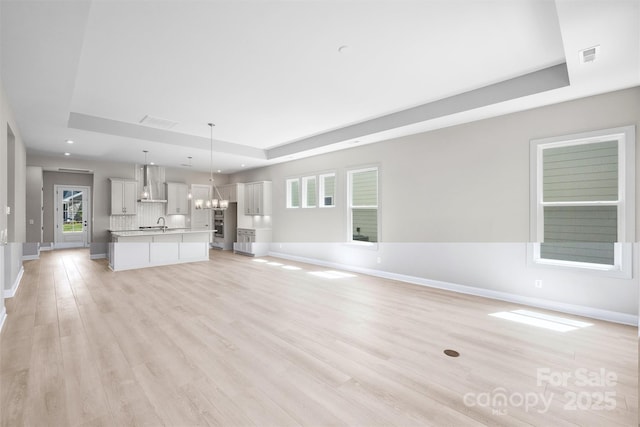 unfurnished living room featuring light wood-style floors, a raised ceiling, a notable chandelier, and baseboards