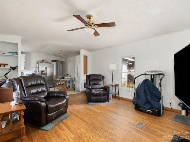 living room with ceiling fan, vaulted ceiling, light hardwood / wood-style floors, and a textured ceiling