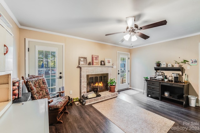 living room with ornamental molding, ceiling fan, a brick fireplace, and dark wood-type flooring