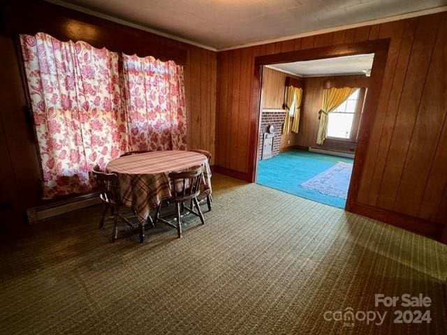 carpeted dining room featuring wood walls, baseboard heating, and crown molding