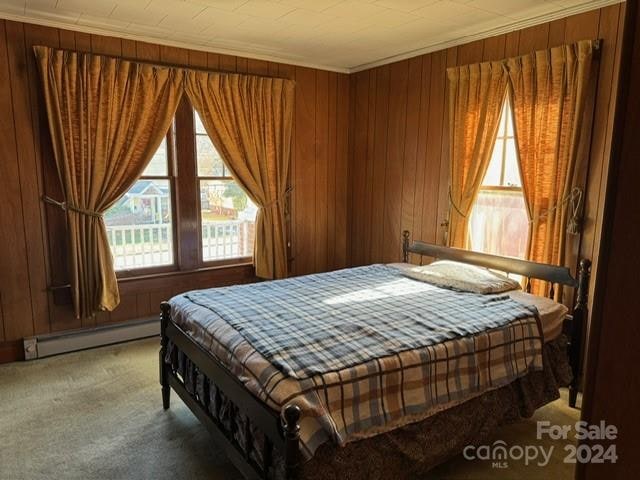 carpeted bedroom with wood walls, a baseboard radiator, and ornamental molding