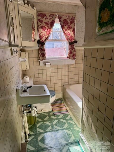 bathroom with toilet, a bath to relax in, tile walls, tile flooring, and sink