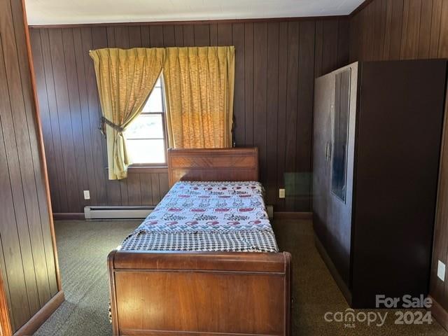 bedroom with wooden walls, dark carpet, and a baseboard heating unit