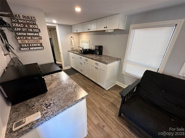 kitchen with sink, dark stone counters, hardwood / wood-style flooring, and white cabinets