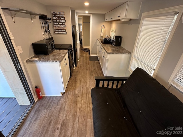 kitchen featuring white cabinets, dark stone counters, black appliances, and light hardwood / wood-style floors