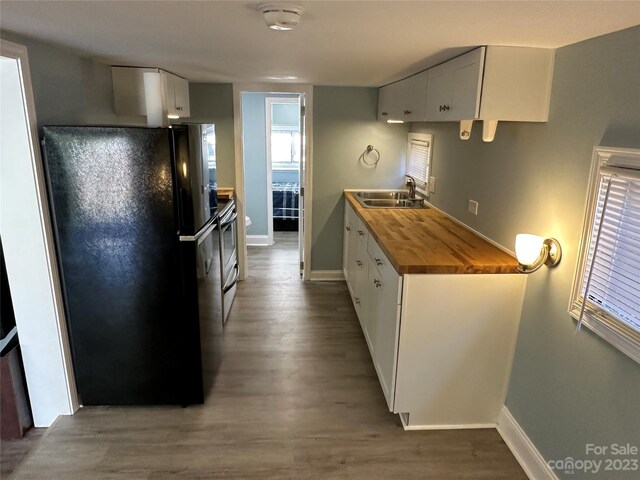 kitchen featuring butcher block countertops, sink, white cabinets, black fridge, and dark hardwood / wood-style flooring