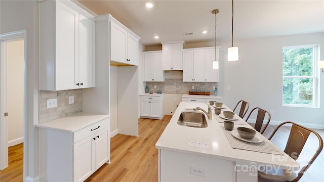 kitchen featuring a center island with sink, white cabinetry, sink, and pendant lighting