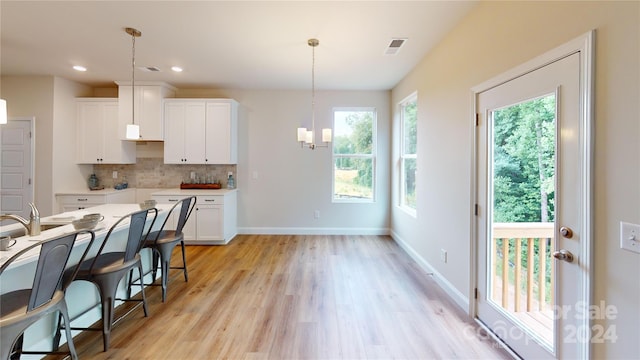 kitchen with white cabinets, decorative backsplash, pendant lighting, and light hardwood / wood-style floors