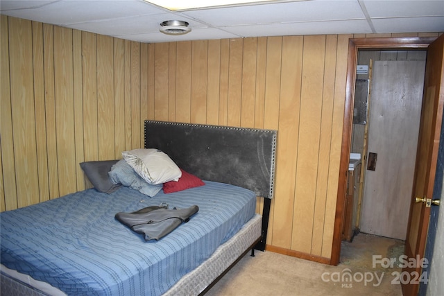 bedroom featuring carpet, wooden walls, and a drop ceiling