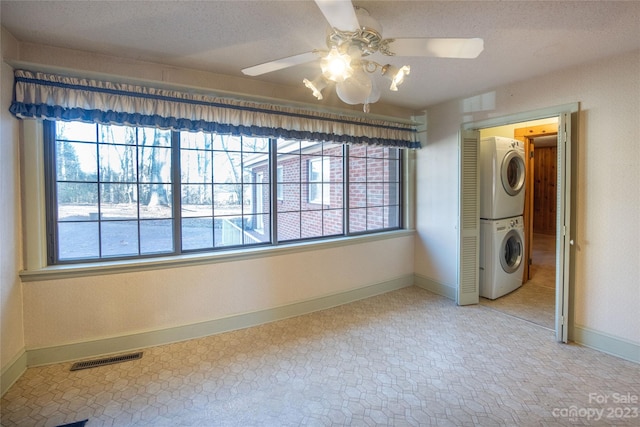 tiled empty room featuring stacked washer and clothes dryer, ceiling fan, and a wealth of natural light