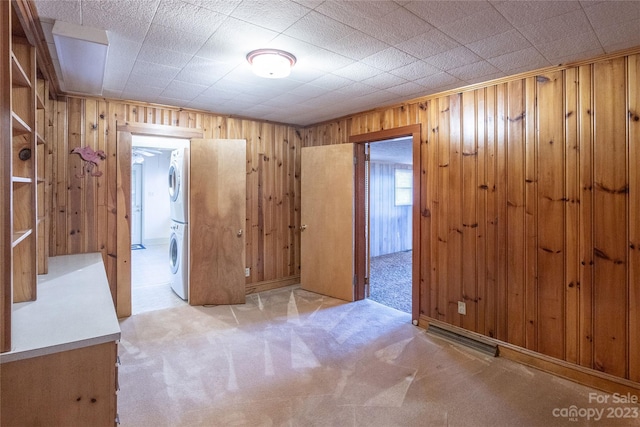 empty room with stacked washer and dryer, light colored carpet, and wooden walls