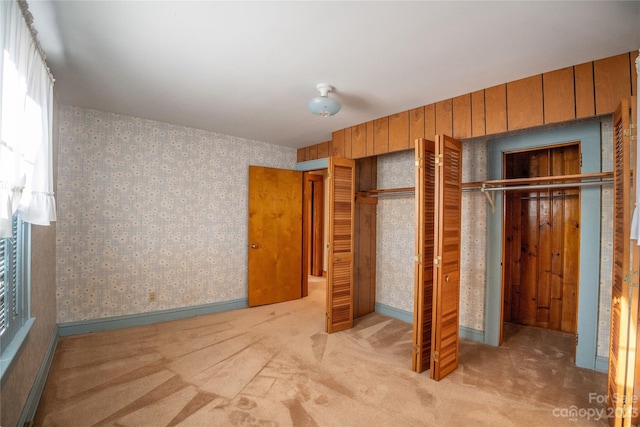 unfurnished bedroom featuring wood walls, a closet, and light colored carpet