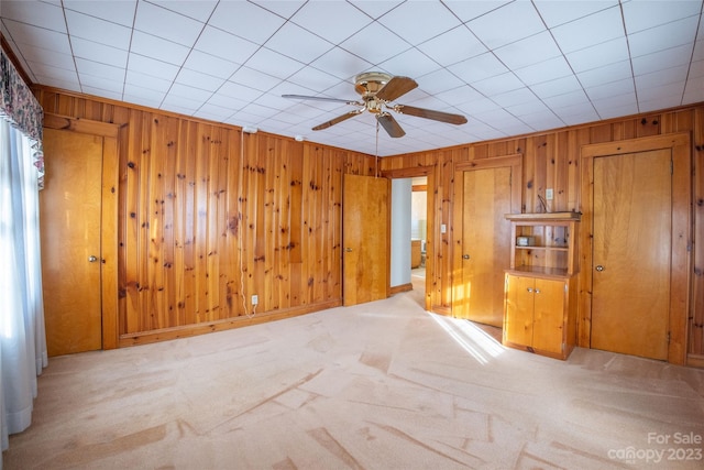 empty room featuring wooden walls, light carpet, and ceiling fan