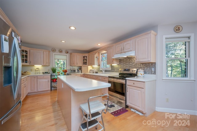 kitchen with backsplash, appliances with stainless steel finishes, a kitchen bar, a kitchen island, and light hardwood / wood-style floors