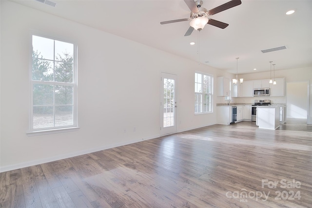 unfurnished living room featuring ceiling fan with notable chandelier and light hardwood / wood-style floors