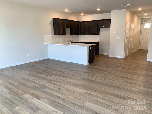 kitchen with dark brown cabinets, light hardwood / wood-style floors, kitchen peninsula, and backsplash