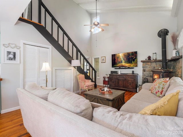 living room featuring ceiling fan, wood-type flooring, a towering ceiling, and a wood stove