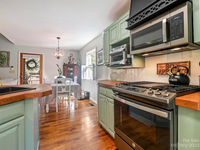 kitchen featuring butcher block countertops, green cabinets, appliances with stainless steel finishes, tasteful backsplash, and decorative light fixtures