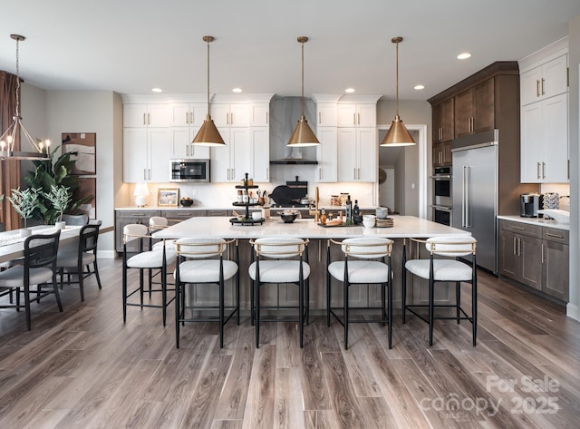 843 Lake Forest Drive Devonshire, Belmont, NC 28012 - kitchen featuring appliances with stainless steel finishes, wall chimney range hood, recessed lighting, wood finished floors, and light countertops