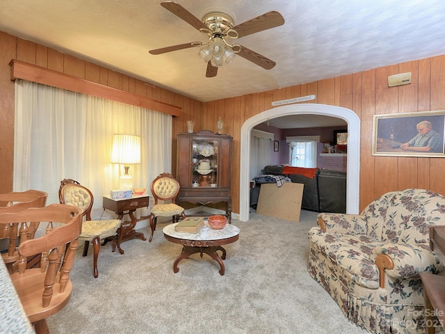 living room featuring ceiling fan, light colored carpet, and wood walls