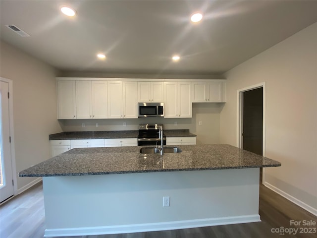 kitchen featuring wood-type flooring, dark stone counters, stainless steel appliances, and an island with sink