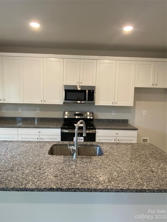 kitchen featuring white cabinets, dark stone counters, appliances with stainless steel finishes, and sink