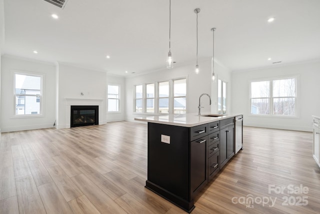 kitchen featuring decorative light fixtures, dishwasher, sink, ornamental molding, and a kitchen island with sink