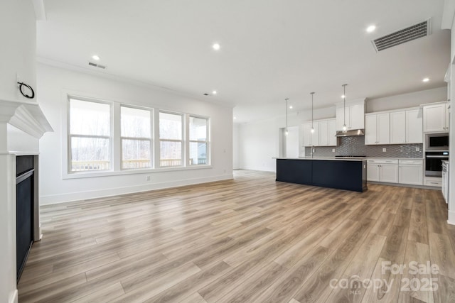 kitchen with decorative light fixtures, white cabinets, decorative backsplash, a kitchen island with sink, and stainless steel appliances