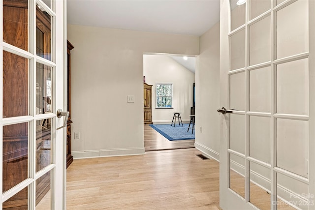 hallway with light wood-type flooring, french doors, and lofted ceiling