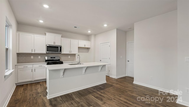 kitchen with stainless steel appliances, an island with sink, white cabinets, sink, and dark hardwood / wood-style flooring