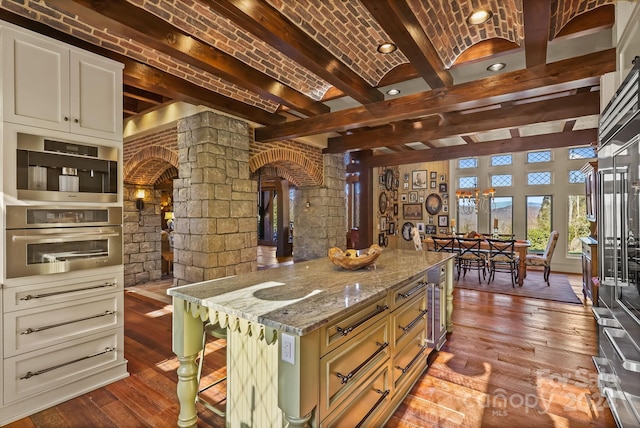 kitchen with a kitchen bar, hardwood / wood-style floors, decorative columns, a kitchen island, and beam ceiling