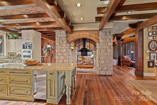 kitchen with light stone countertops, wood-type flooring, a wood stove, and beam ceiling